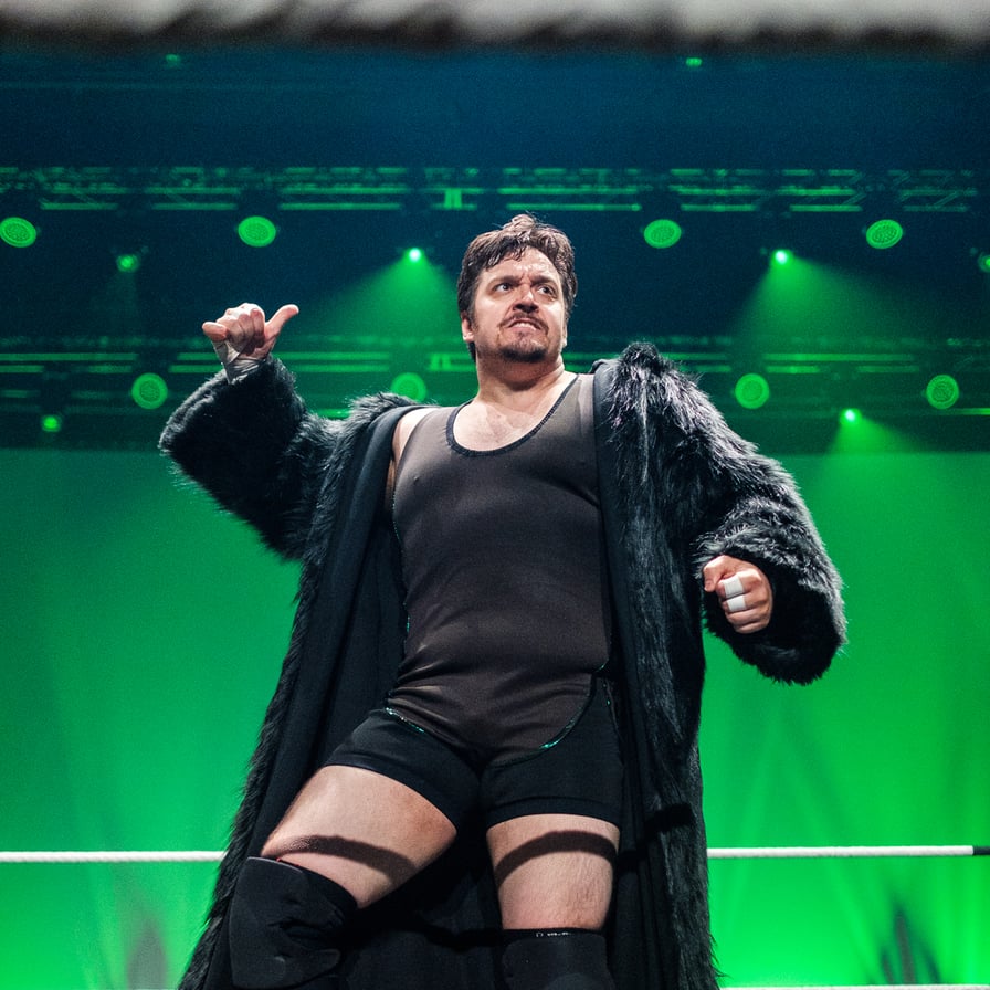 Kuva Juhana Karhulasta painimatolla. Hänellä on päällään musta trikoopaita ja pitkä turkisreunainen takki, taustalla vihreät lavavalot. Kuva: FCF Wrestling / Akseli Vaheristo.