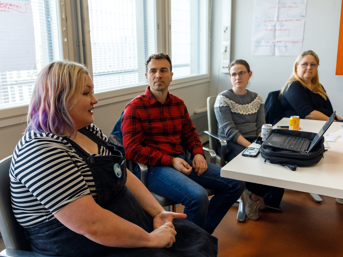 Four campaign team members in discussion around a meeting table, with handwritten flip-chart sheets on the wall behind them.