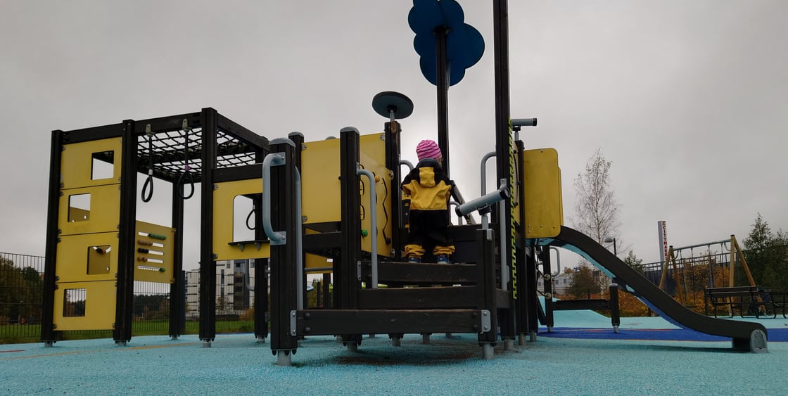 Pieni lapsi haalari päällä kiipeämässä leikkitelineeseen, jossa on liukumäki ja erinäisiä kiipeilytelineitä