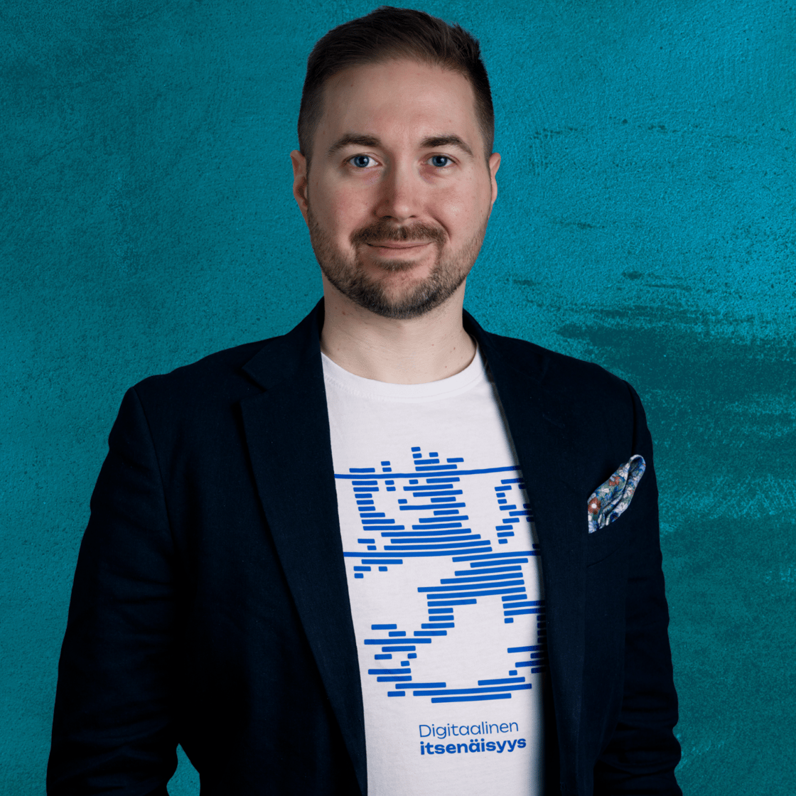 Lauri Lavanti smiling and looking at the camera. He is wearing a white t-shirt that reads Digitaalinen itsenäisyys (Digital independence) with a lion motif above it, and a blazer. Photo by Erkki Laine.