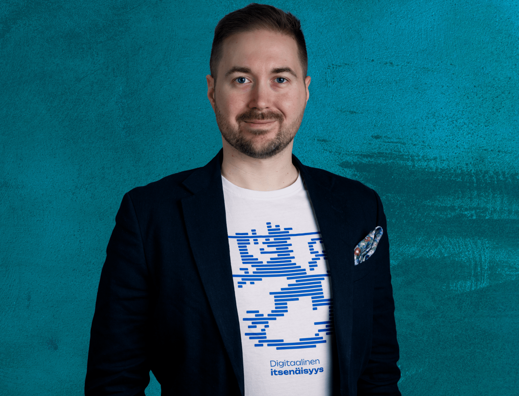 Lauri Lavanti smiling and looking at the camera. He is wearing a white t-shirt reading Digitaalinen itsenäisyys with a lion emblem above it, and a blazer. Photo by Erkki Laine.