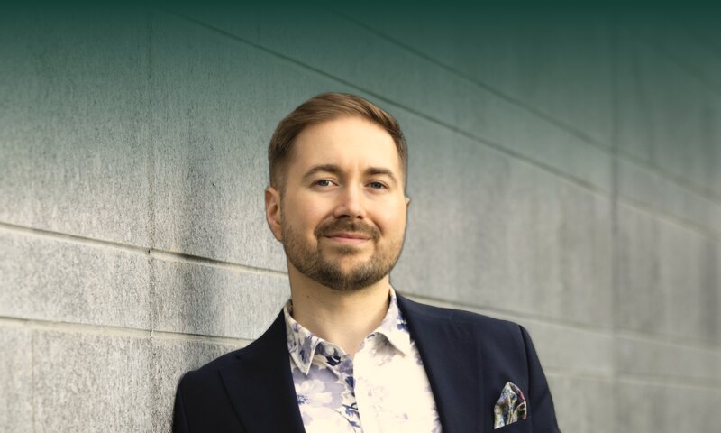 Lauri Lavanti nojaa graniittimuuriin toinen käsi taskussa ja katsoo kameraan, yllään tummansininen pikkutakki ja kukkakuvioinen paita.