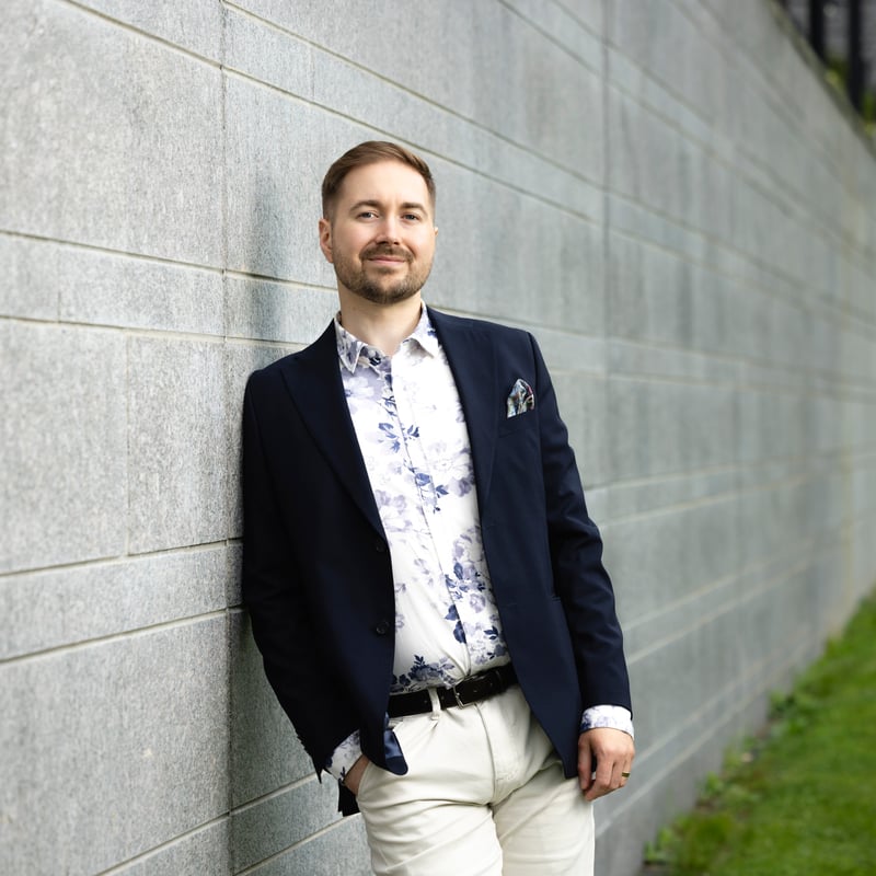 Lauri Lavanti nojaa graniittimuuriin toinen käsi taskussa ja katsoo kameraan, yllään tummansininen pikkutakki, kukkakuvioinen paita ja vaaleat housut.