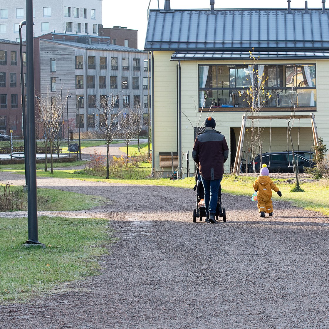 Lauri Lavanti pushing a pram on a gravel path, a child walking beside him and houses in the background.