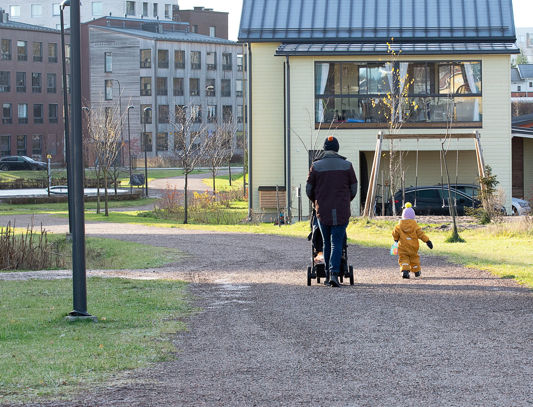 Lauri Lavanti pushing a pram on a gravel path, a child walking beside him and houses in the background.