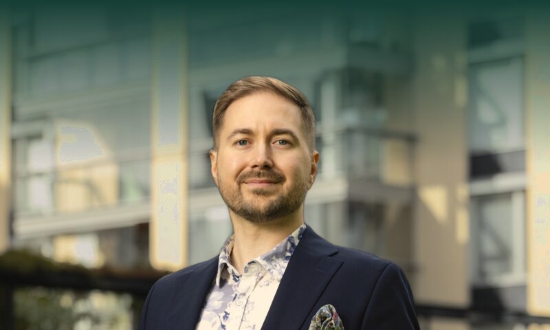Lauri Lavanti seisoo nurmikolla kerrostalojen edessä kädet taskuissa, yllään tummansininen pikkutakki ja kukkakuvioinen paita.