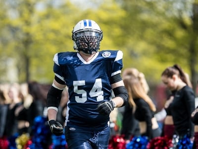 Lauri Lavanti in a navy number 54 jersey and helmet running onto the field, cheerleaders blurred behind him.