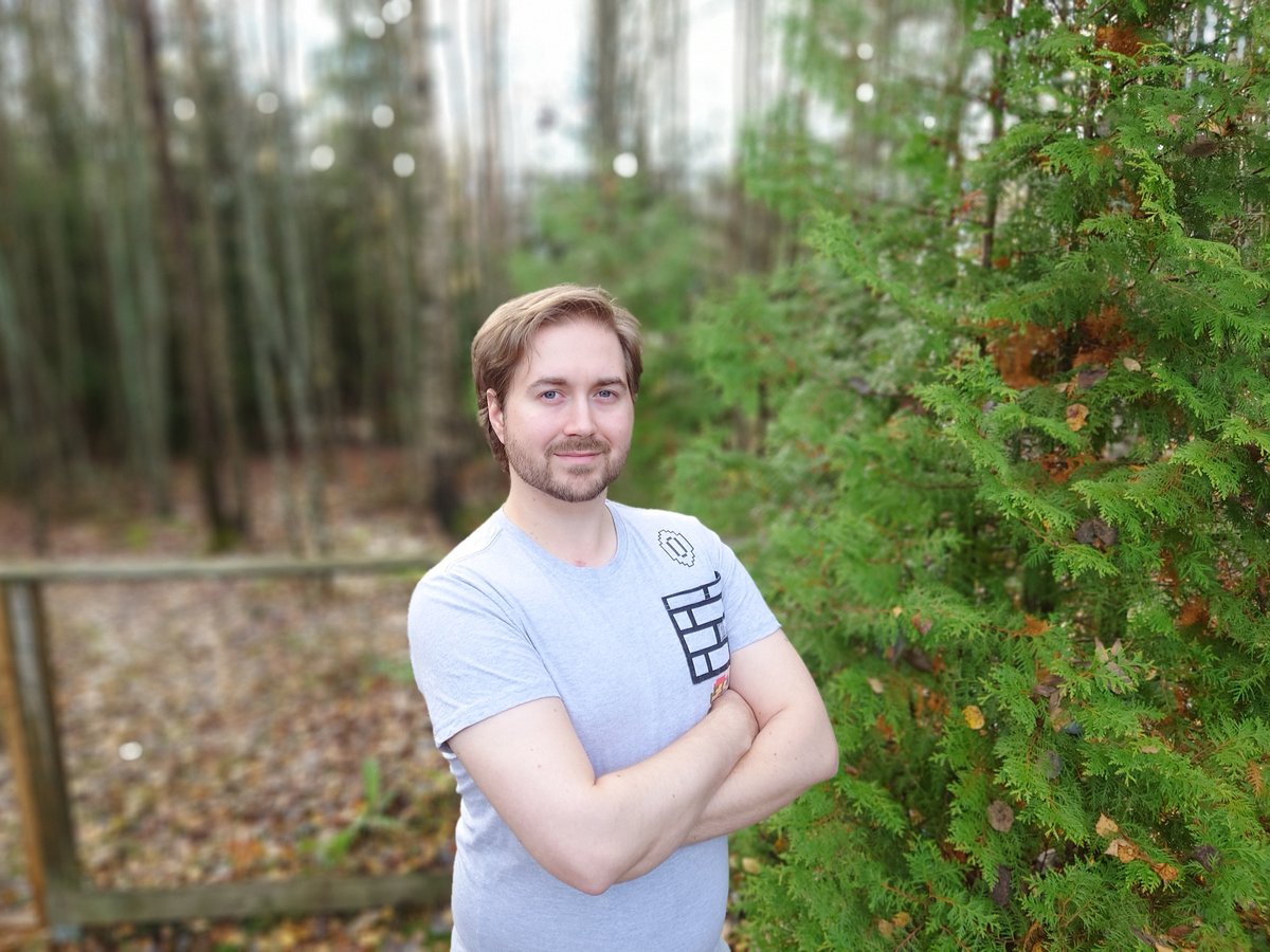 Lauri Lavanti in a light t-shirt with arms crossed, smiling in an autumn birch and spruce forest.