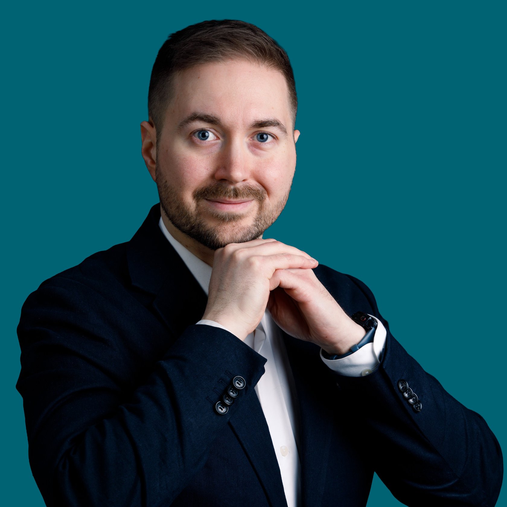 Lauri Lavanti resting his hands against each other and looking at the camera with a smile. He is wearing a white dress shirt and a dark blazer. Photo by Erkki Laine.