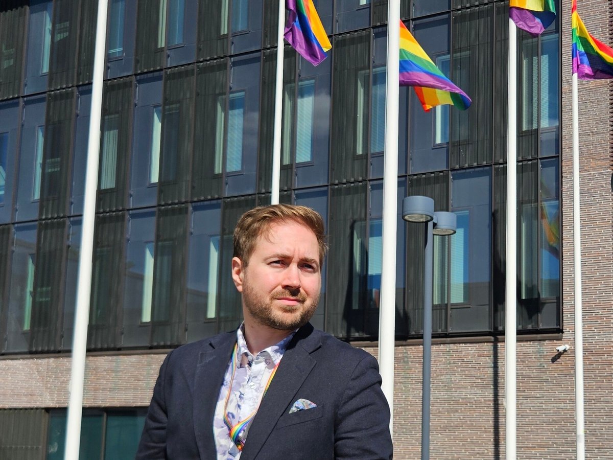 Lauri Lavanti in front of Kirkkonummi town hall, rainbow flags flying on the flagpoles above him.