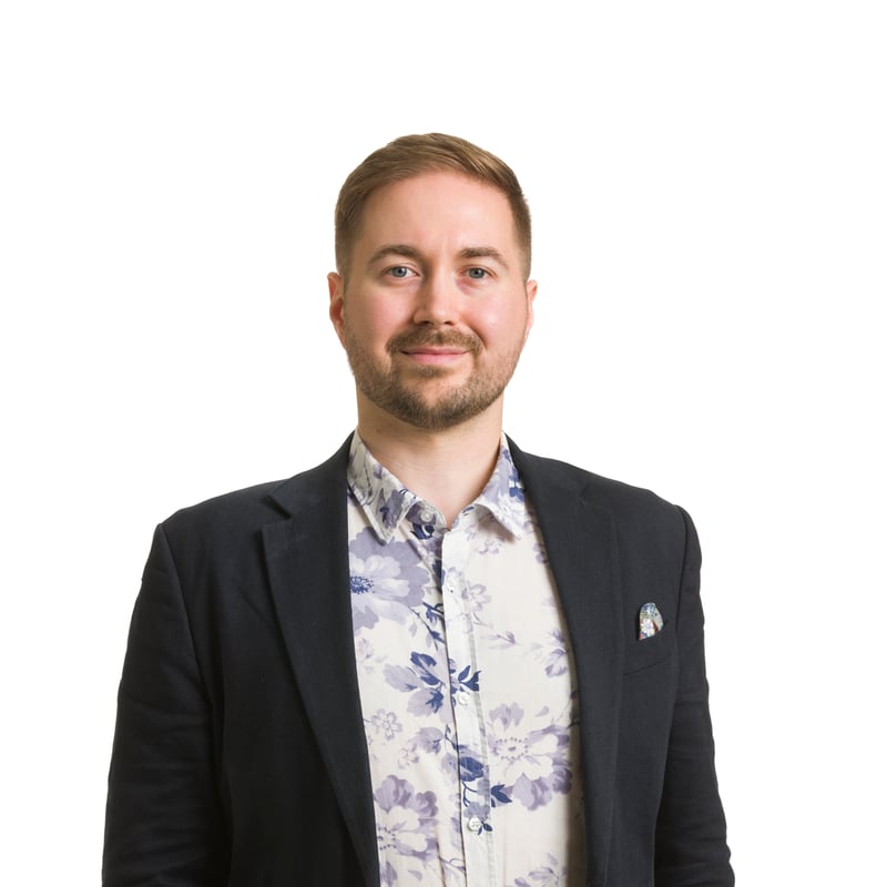 Studiokuva Lauri Lavannista valkoista taustaa vasten, takki auki ja pieni rintamerkki näkyvissä rinnuksessa, yllään tummansininen pikkutakki ja kukkakuvioinen paita.