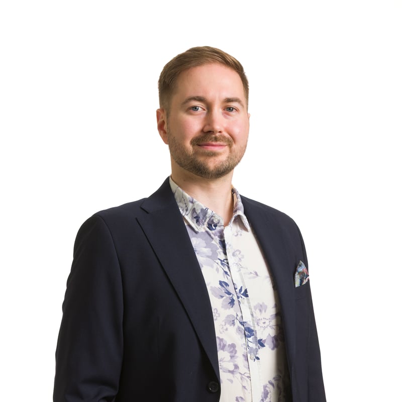 Studiokuva Lauri Lavannista valkoista taustaa vasten, seisoo hieman sivuttain toinen käsi taskussa, yllään tummansininen pikkutakki ja kukkakuvioinen paita.