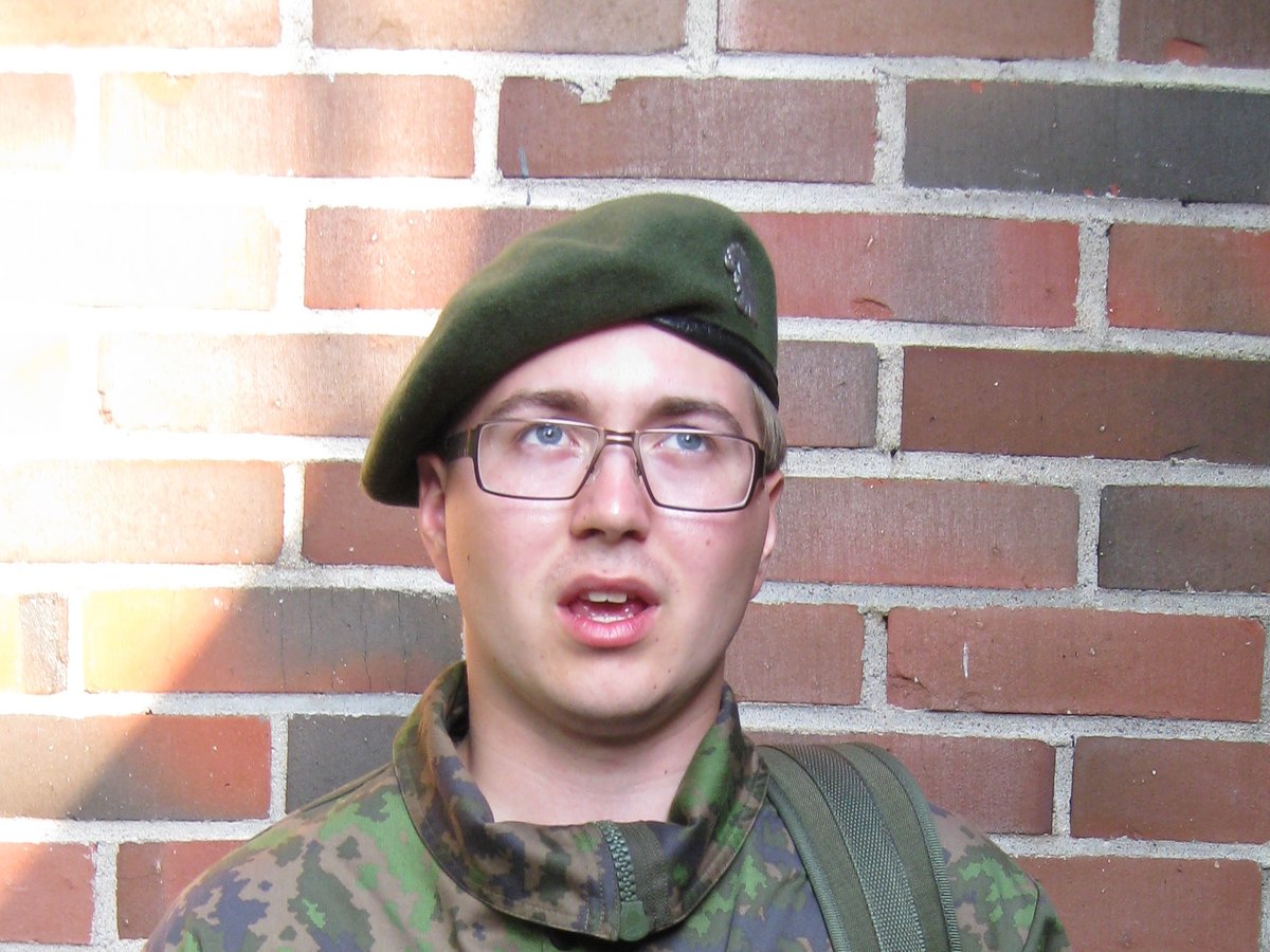 Lauri Lavanti in a green beret and camouflage uniform in front of a red-brick barracks wall.