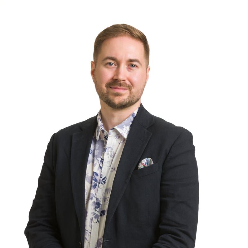 Virallinen studiokuva Lauri Lavannista valkoista taustaa vasten, kädet yhdessä edessä, yllään tummansininen pikkutakki ja kukkakuvioinen paita.