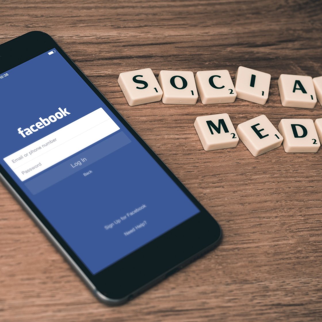 A phone with the Facebook app open waiting for login credentials, and the text "Social media" made from Scrabble tiles.