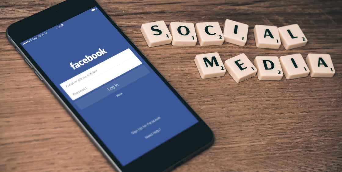 Puhelin, jossa on auki Facebookin sovellus odottamassa kirjautumistietoja sekä Scrabble-pelistä tutuilla nappuloilla tehty teksti "Social media"