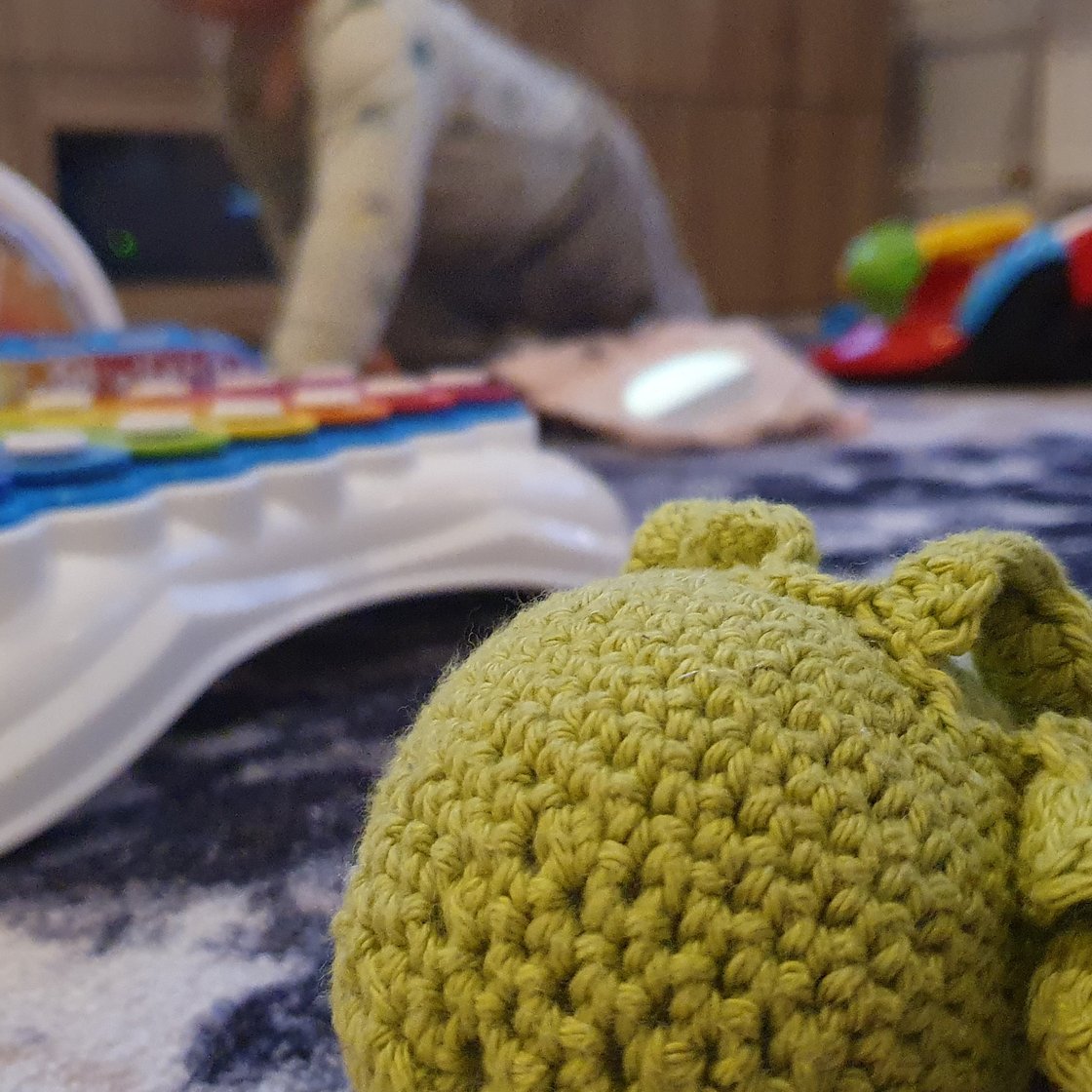 A knitted soft toy, with various children's toys in the background.