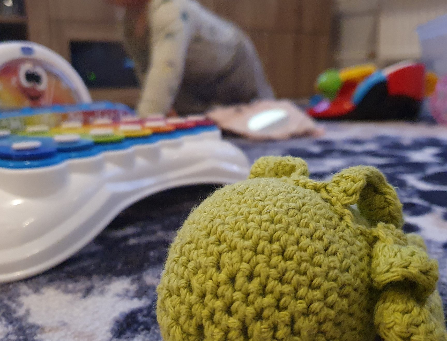 A knitted soft toy, with various children's toys in the background.
