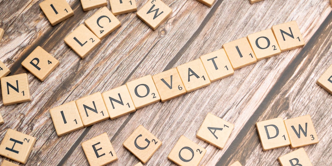 Scrabble-pelin puupalikoita puupöydällä, keskellä palikoista muodostettu sana innovation.