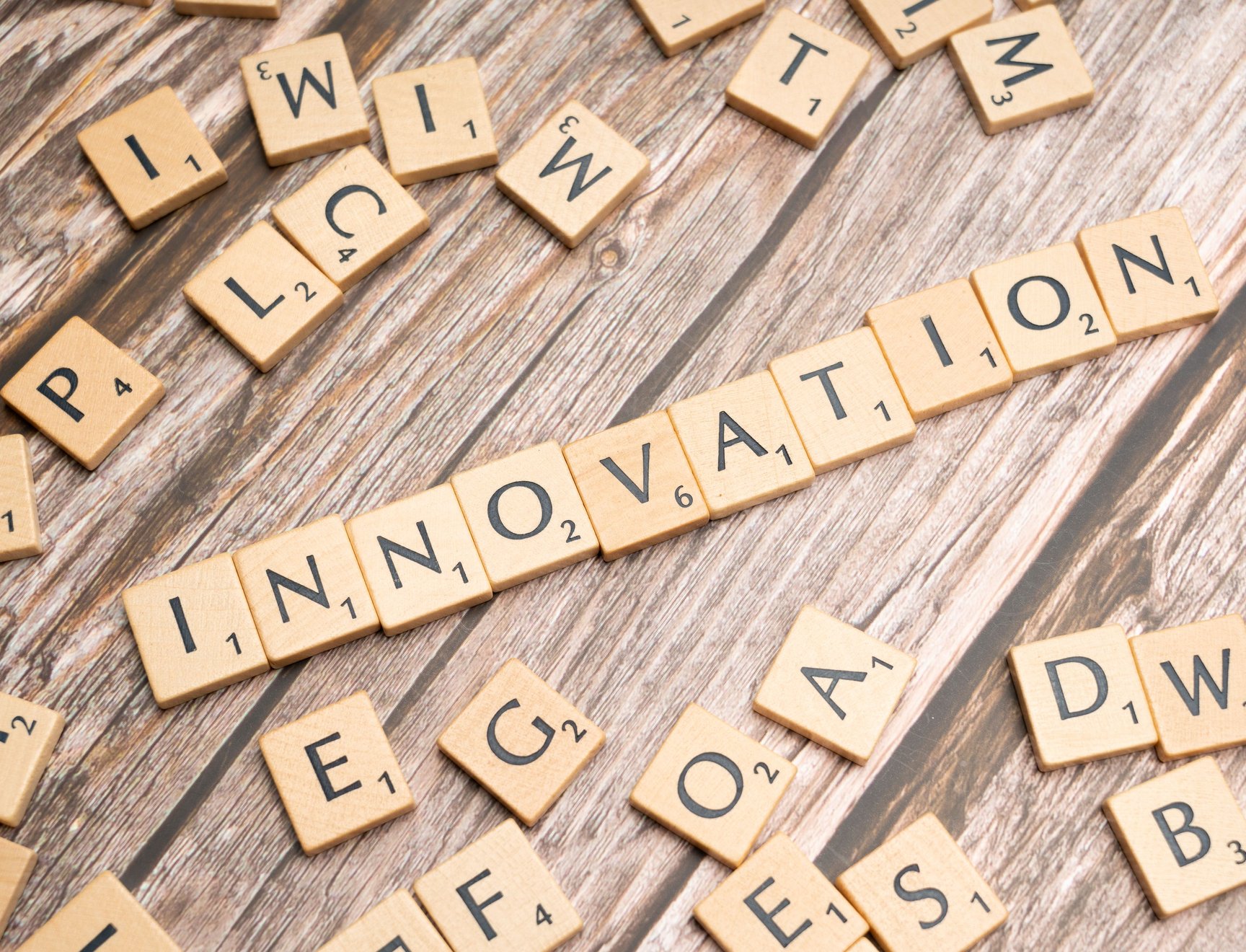 Scrabble-pelin puupalikoita puupöydällä, keskellä palikoista muodostettu sana innovation.