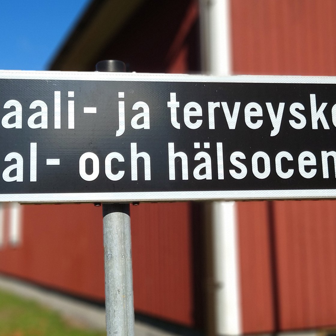 A road sign reading "Sosiaali- ja terveyskeskus" (Social and health centre) and below it the same text in Swedish: "Social- och hälsocentral".